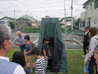 テントを張ったマンホールトイレを見学する子どもたちの写真