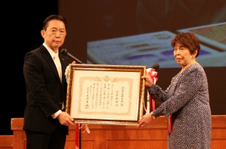 名誉市民証を掲げる後藤恂子さんと井崎市長の写真