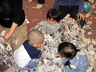 新聞紙に埋もれて遊ぶ子どもたちの写真