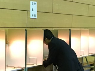 本番と同じ投票台で投票用紙に記入する生徒の写真