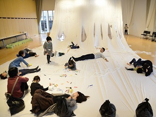 写真：大きな白い布に寝転がる参加者