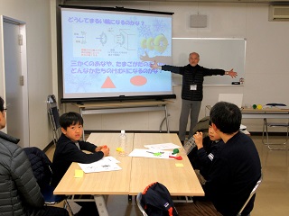 写真：空気砲の玉が丸くなる原理について説明を聞く子ども達