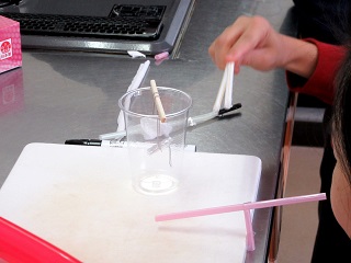 写真：透明なコップにつるしたアルミホイルの振り子を静電気の力で動かす実験