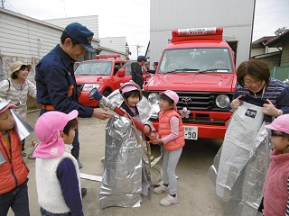 写真：防火服身につけ、実際に使用しているホースを持つ体験をする子ども達