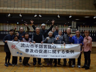 写真：条例が可決され歓喜する聴覚障害者団体の「流山市デフ協会」の皆さんや関係者の方々