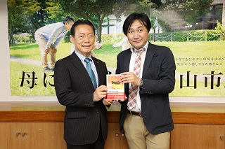 豊田さんから本を受け取る井崎市長
