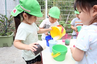 子どもがバケツの中の水をカップに注ぎ、カップから溢れている