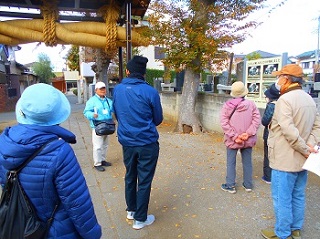 鳥居の前でガイドの方の話をきく参加者の方々の様子の写真。鳥居にはしめ縄が見える