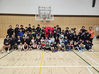 バスケットボール講習会の集合写真（子どもから大人、ちーばくんがバスケットゴールの前で集合している写真）