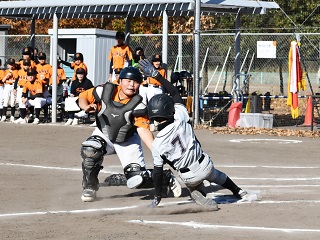 東深井ボーイズの背番号7番の選手がホームベースにスライディングし、流山ホークスのキャッチャーがタッチしようとしている様子の写真