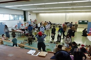 広い会場の壁沿いに机やシートが敷かれ、さまざまなイベントコーナーがある様子がわかる会場全体の写真