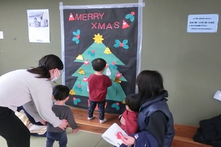 壁に色画用紙で作られたクリスマスツリーが張られており、そのツリーに雪だるまの折り紙を張っている男の子の写真