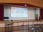 体育館の檀上にスクリーンがでており、画面に全国中学校駅伝大会と表示されている写真