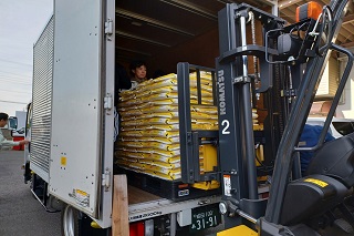 寄付された無洗米を重機でトラックに運んでいる様子の写真