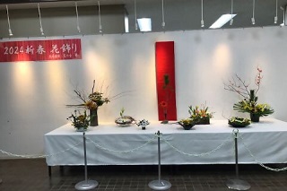 「2024新春花飾り」と書かれた幕の前に作品が並んでいる様子の写真