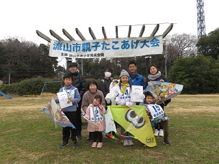 流山市親子たこあげ大会と書かれた横断幕の前で、たこと一緒に写真をとる受賞者の集合写真