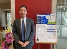 講演のポスターを背に微笑む古田先生