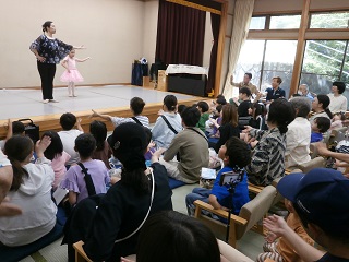 バレエの講師が舞台の上から来場者に向かってバレエの振り付けを説明