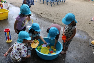 子ども達が水を張ったたらいの周りに集まり水遊びをしている。