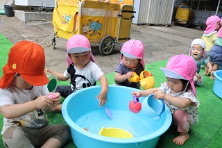 1歳児と2歳児の子どもがたらいに張った水をスプーンですくったりしながら遊んでいる