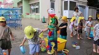 子ども達が玩具の水車を重ねて上から水を流している