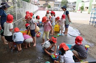5歳児クラスの子ども達がたらいの周りで水遊びをしている。