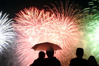 小雨に傘をさし花火を見るカップルの写真