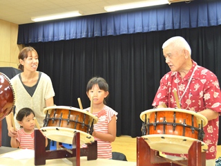 高野瀬さん親子に太鼓を教える中村さんの写真