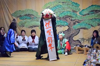 「謹賀新年」と書かれた半紙をくわえる獅子舞の写真