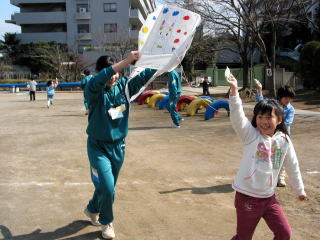 中学生と一緒に凧揚げをする小学生の写真
